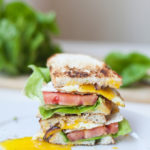 Fried egg blt cut in half and stacked on top of each other on a plate.