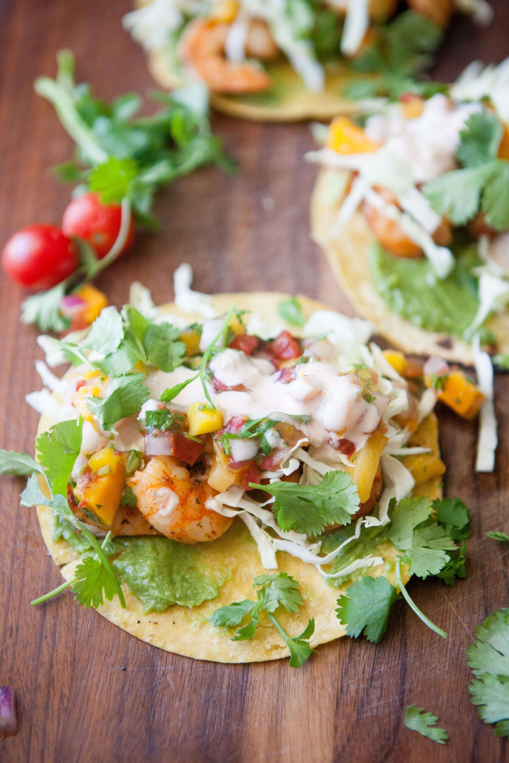 Three shrimp tacos topped with mango salsa and cilantro on top of wood board.