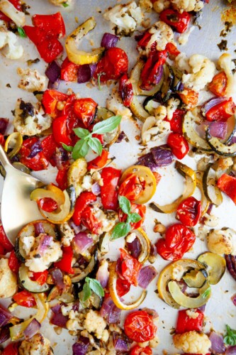 Roasted basil veggies cooked on sheet pan with gold spoon.