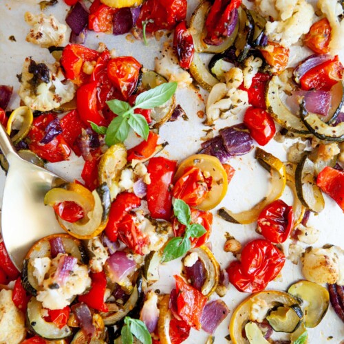 Roasted basil veggies cooked on sheet pan with gold spoon.
