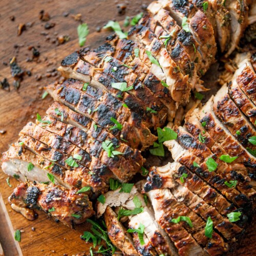 Balsamic and herb pork tenderloin sliced and garnished with fresh herbs.