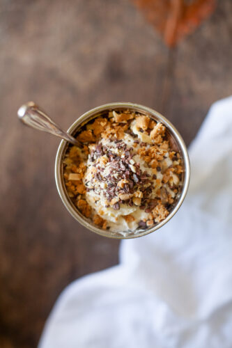 A cup of a frosty protein shake topped with rice crispies, chocolate nibs, whipped cream, protein bars, and more!