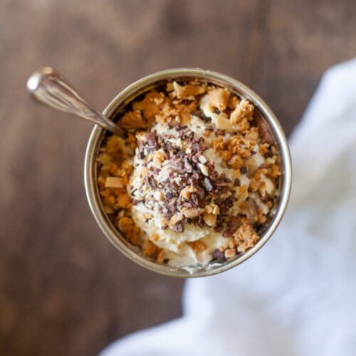 A cup of a frosty protein shake topped with rice crispies, chocolate nibs, whipped cream, protein bars, and more!