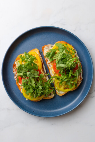 Two tomato basil egg white toasts topped with arugula on blue plate.