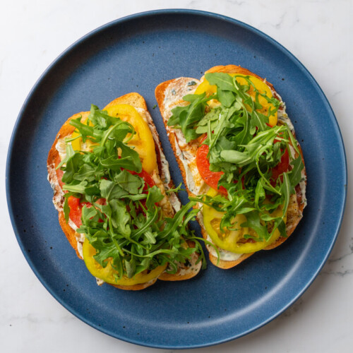 Two tomato basil egg white toasts topped with arugula on blue plate.