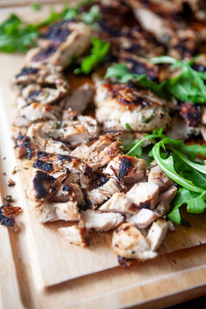 Herb marinated chicken thighs grilled and sliced on wood cutting board.