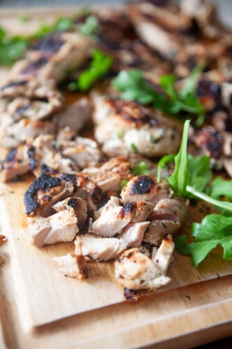 Herb marinated chicken thighs chopped on wood cutting board.