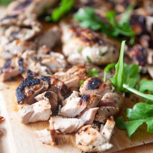 Herb marinated chicken thighs chopped on wood cutting board.