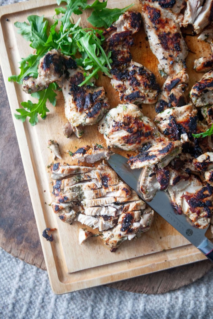 Herb marinated chicken thighs cooked and cut on wooden cutting board.