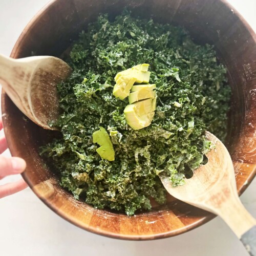 Kale caesar salad prepared and tossed in wooden salad bowl.