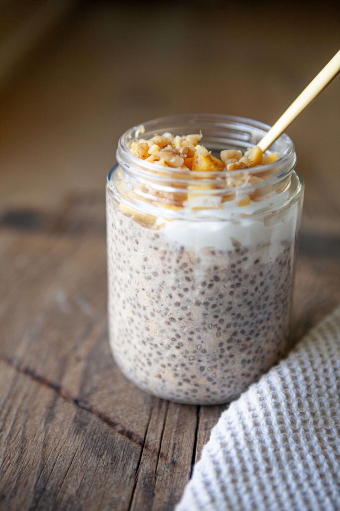 Overnight oats with mango and walnuts made in a jar with gold spoon digging inside.