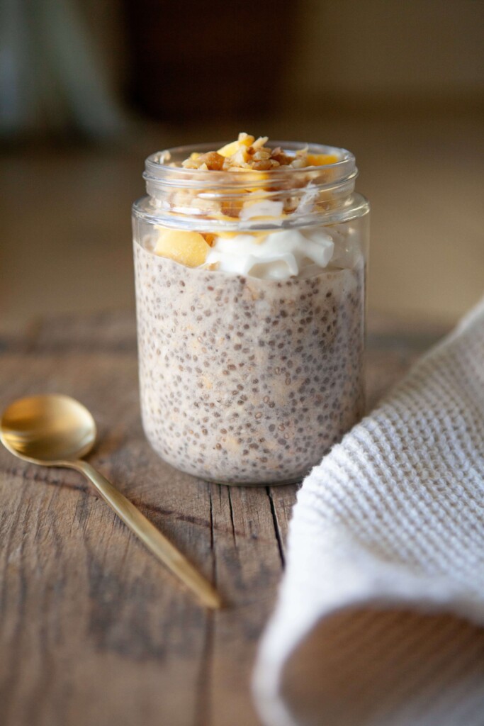 Overnight oats topped with mango and walnuts with spoon on the left side of jar.