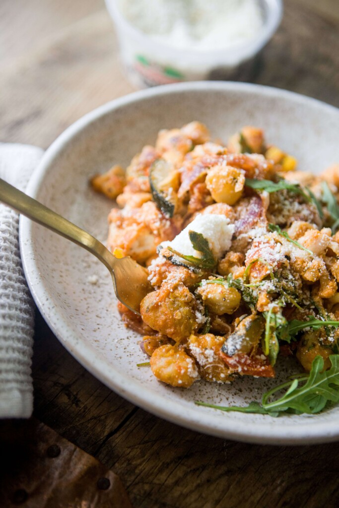 Sheet pan gnocchi dinner in a bowl with gold fork digging into it.