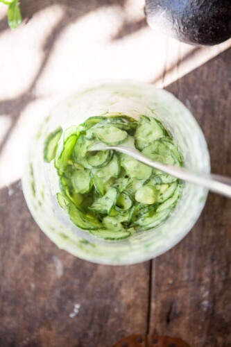 Cucumber salad mixed together in large plastic container.
