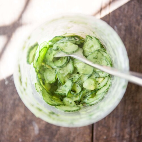 Cucumber salad mixed together in large plastic container.