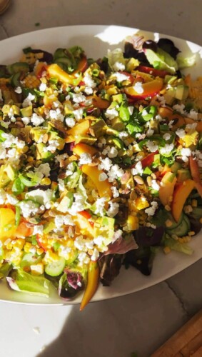 Summer, peach, corn and goat cheese salad assembled in a large white bowl.