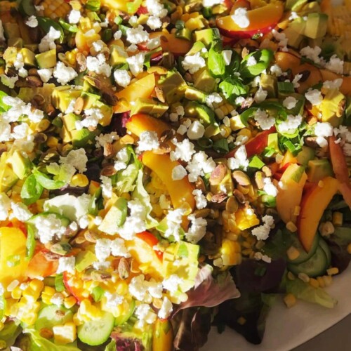 Summer, peach, corn and goat cheese salad assembled in a large white bowl.
