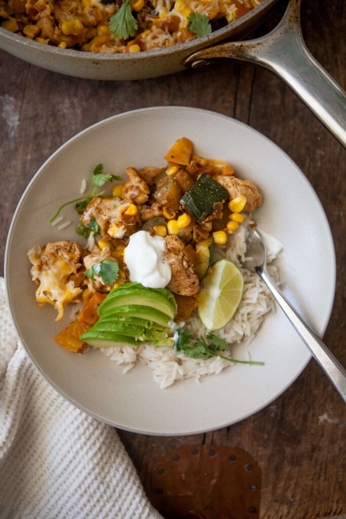 Zucchini, corn and chicken skillet served in a bowl sour cream and avocado.