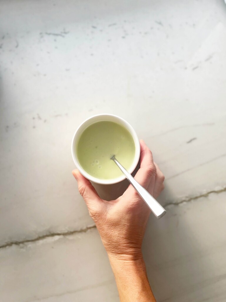 Hand holding small bowl of avocado caesar dressing.