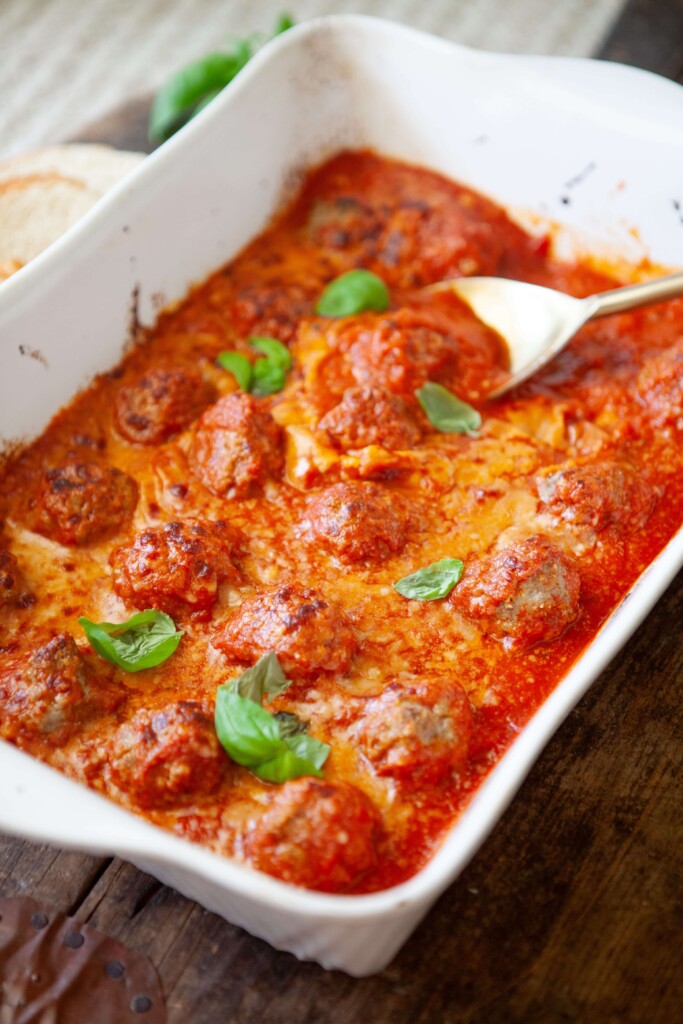 Spoon scooping up a cottage cheese meatball out of 9x13 pan.