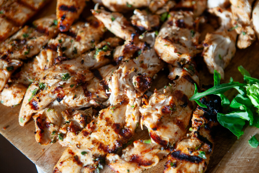 Marinated grilled chicken cut into strips on a wooden cutting board.