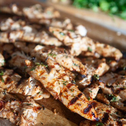 Marinated grilled chicken on a wooden cutting board cut into strips.