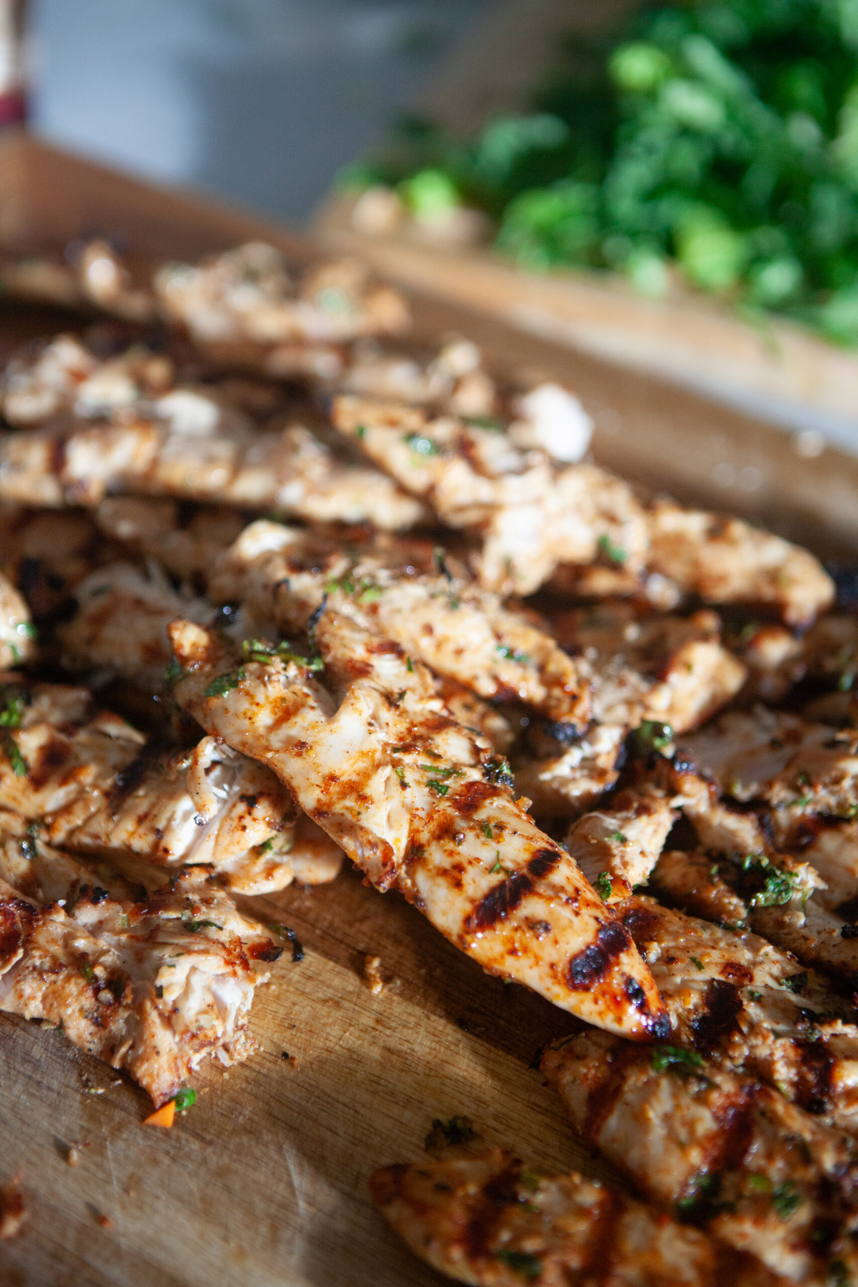 Marinated grilled chicken on a wooden cutting board cut into strips.