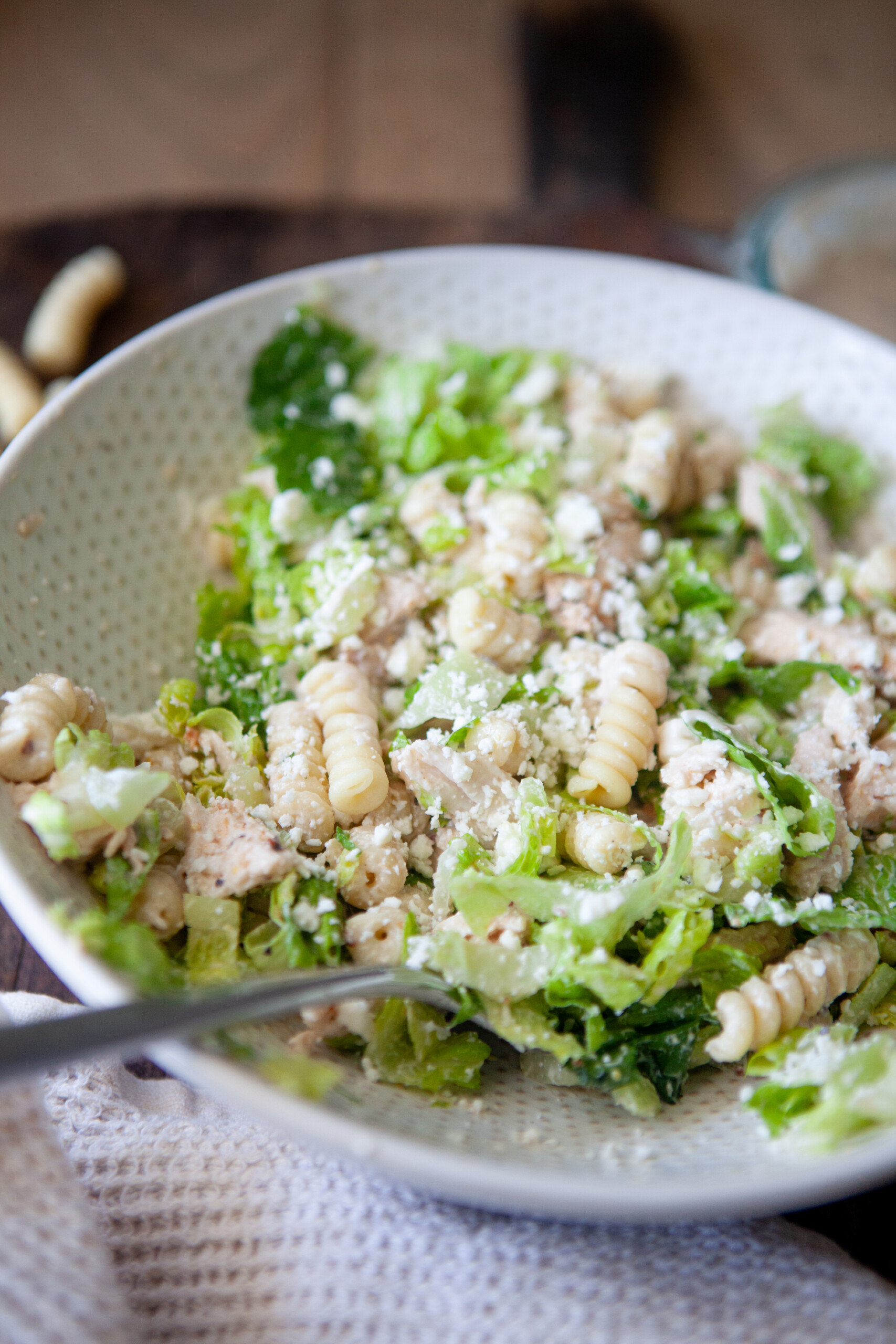A serving of Caesar pasta salad in a white bowl with a fork.