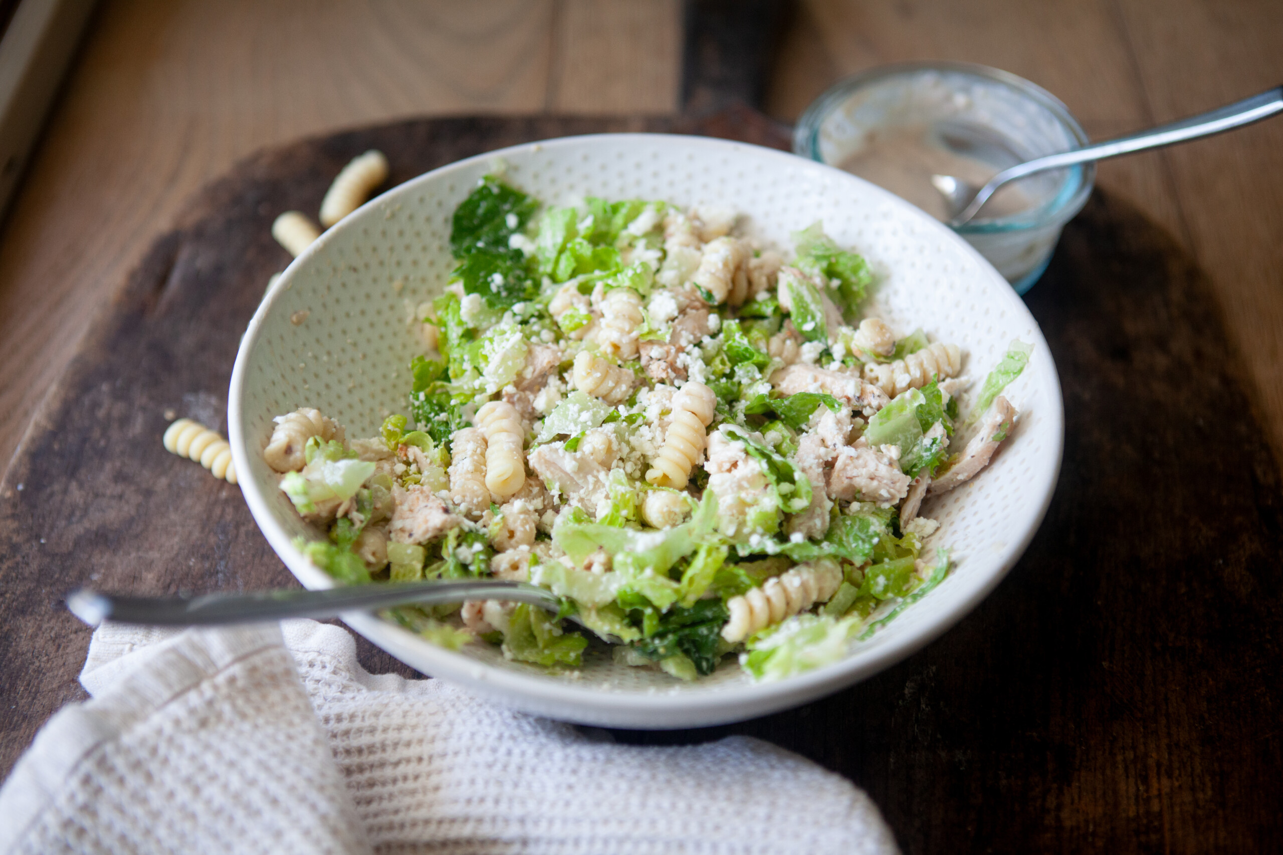A serving of Caesar pasta salad in a white bowl.