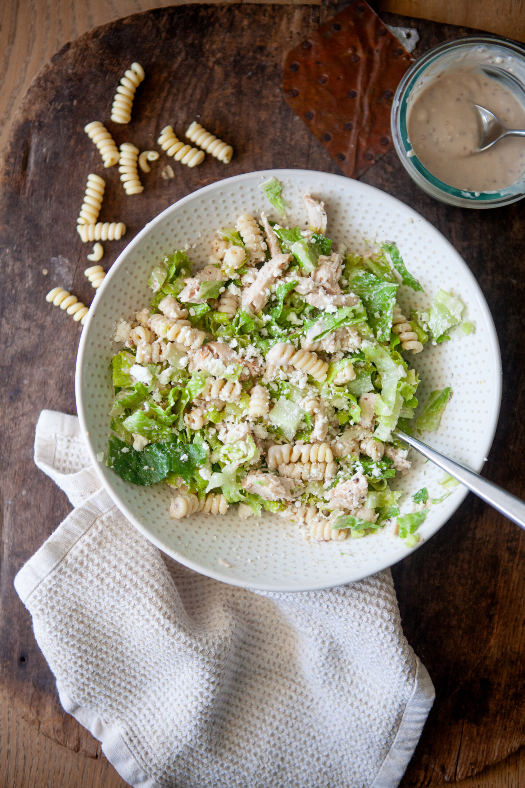 Caesar pasta salad in a white bowl on a wooden table.