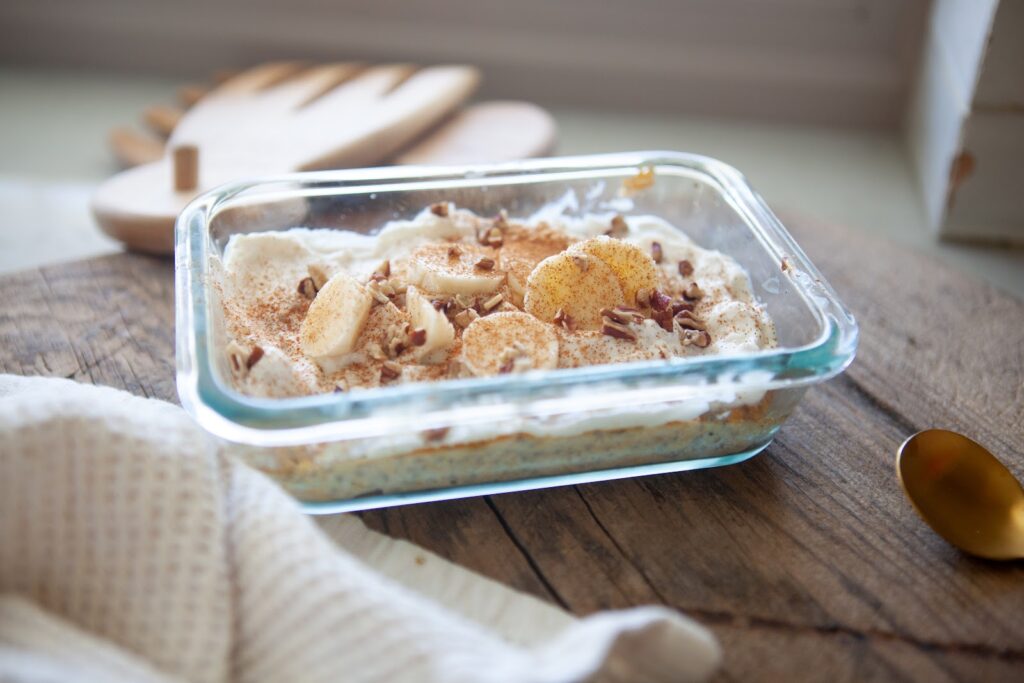 Side view of a high protein banana butternut baked oat bowl with toppings in a glass container on a wooden board