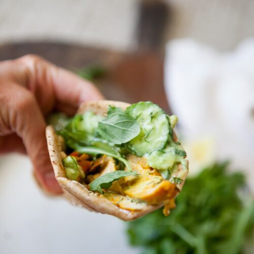 Close-up of a chicken shawarma pita with creamy cucumber salad, dill, and arugula
