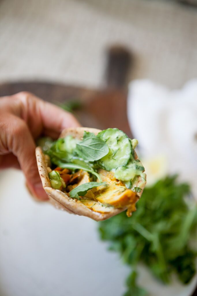 Close-up of a chicken shawarma pita with creamy cucumber salad, dill, and arugula