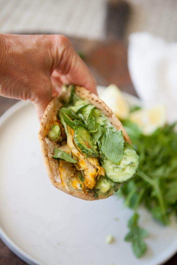 Chicken shawarma pita held up to show sliced cucumbers, avocado, and shawarma chicken inside