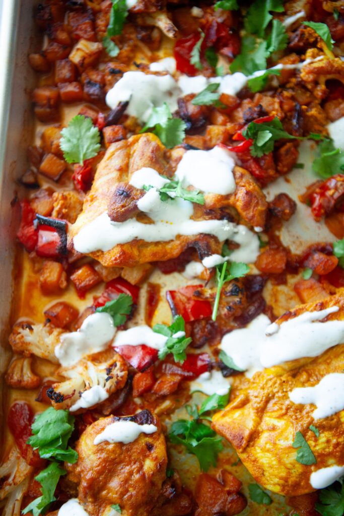 Close-up of turmeric and paprika spiced chicken thighs on roasted vegetables with a Greek yogurt drizzle and fresh cilantro