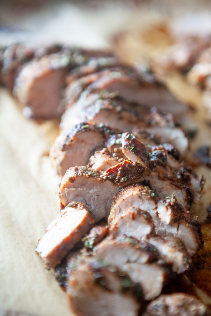 Sliced BBQ pork tenderloin on a parchment-lined sheet pan right out of the oven