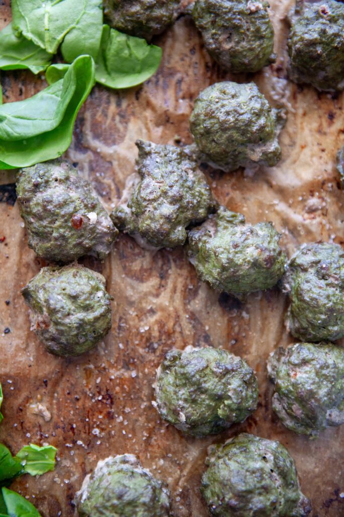 Picking up a spinach basil meatball with a fork from the baking sheet