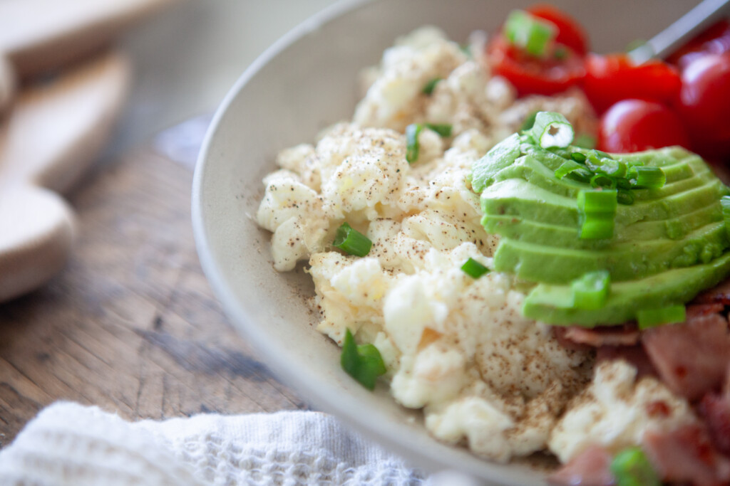 A bowl of scrambled egg whites topped with sliced avocado, cherry tomatoes, and chopped green onions
